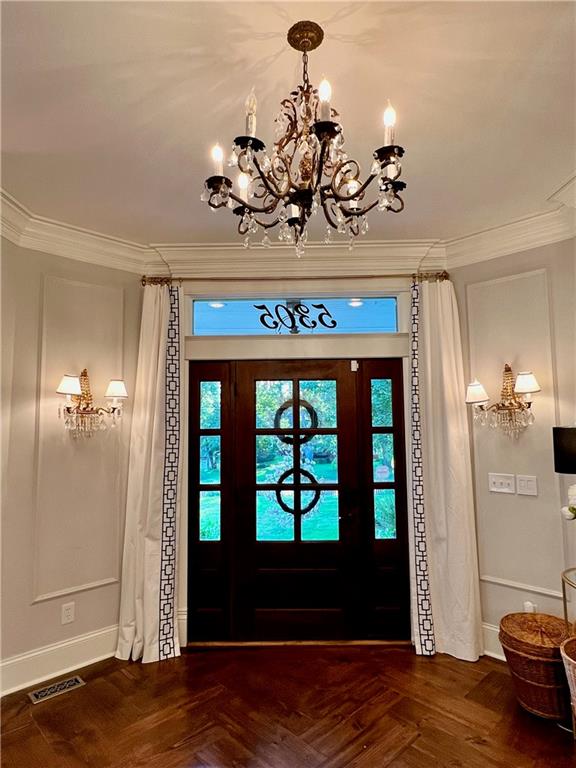 entryway featuring crown molding, a notable chandelier, and parquet floors