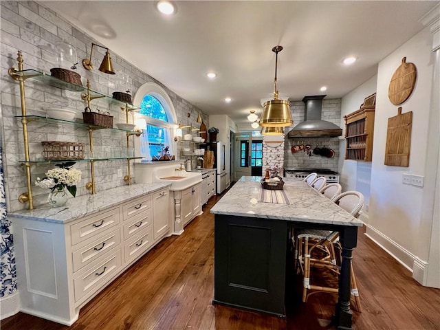 kitchen featuring wall chimney exhaust hood, a kitchen island, a kitchen bar, white cabinetry, and dark hardwood / wood-style floors