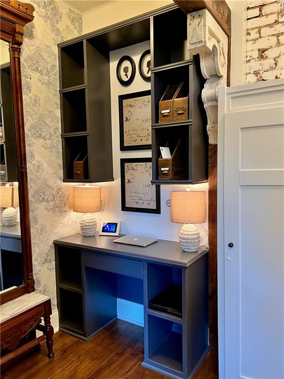 unfurnished office featuring crown molding, built in desk, and dark wood-type flooring