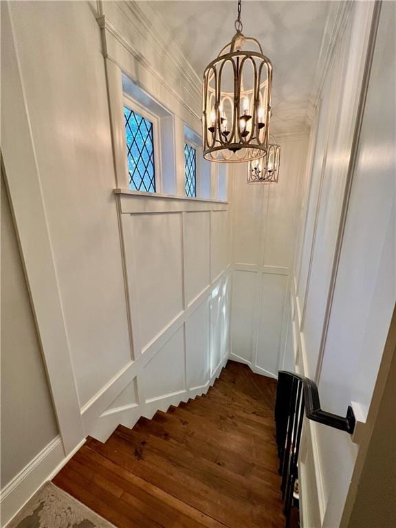 staircase featuring dark wood-type flooring, a chandelier, and ornamental molding