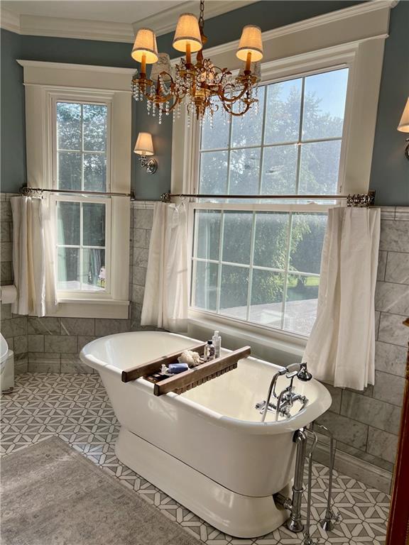 bathroom featuring a bath to relax in, ornamental molding, a notable chandelier, and tile flooring