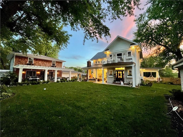 back house at dusk with a balcony, a pergola, a yard, and a patio area