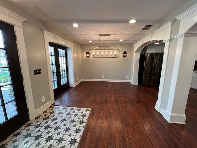 foyer entrance with french doors, a notable chandelier, dark hardwood / wood-style floors, and decorative columns