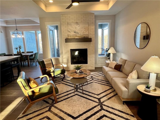 living room with crown molding, dark wood-type flooring, a fireplace, and a tray ceiling