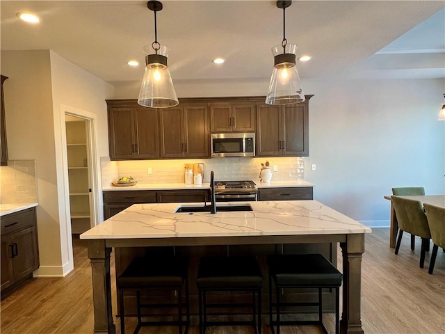 kitchen with stainless steel appliances, light hardwood / wood-style flooring, tasteful backsplash, and an island with sink