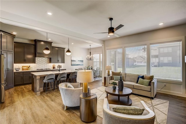 living room with light wood-type flooring, a wealth of natural light, recessed lighting, and ceiling fan with notable chandelier