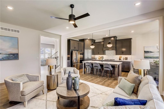 living room featuring light wood finished floors, visible vents, a ceiling fan, stairs, and recessed lighting