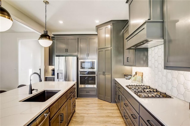 kitchen featuring hanging light fixtures, light stone countertops, stainless steel appliances, light wood-type flooring, and a sink