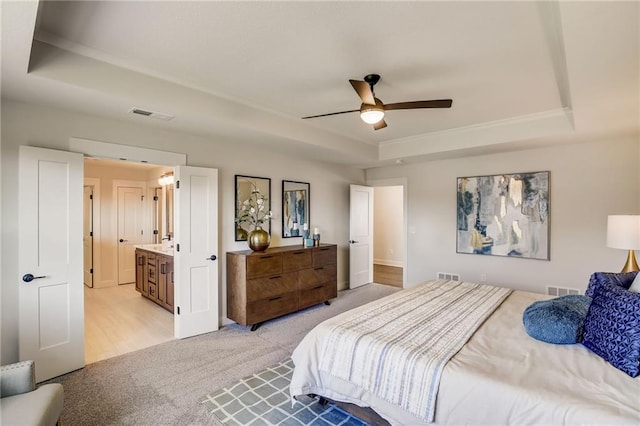 bedroom featuring light carpet, a tray ceiling, visible vents, and a ceiling fan