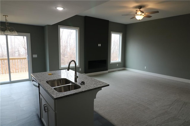 kitchen with sink, dishwasher, light stone counters, pendant lighting, and a kitchen island with sink