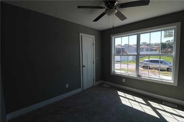 unfurnished room with a wealth of natural light, ceiling fan, and dark carpet