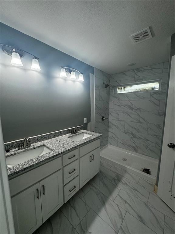 bathroom featuring a tile shower, vanity, and a textured ceiling