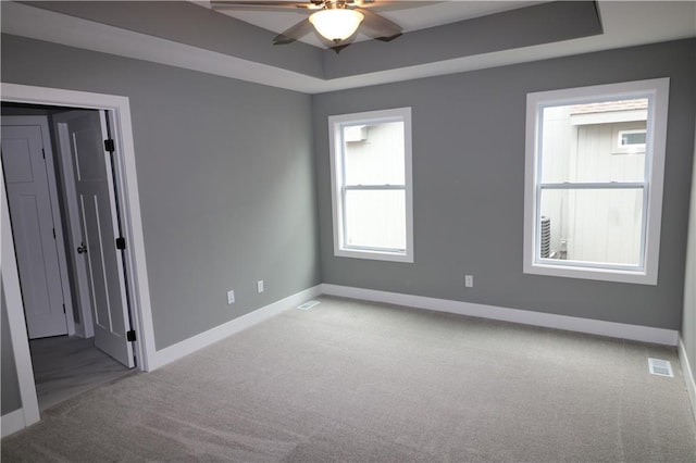 spare room with a tray ceiling, ceiling fan, and light colored carpet