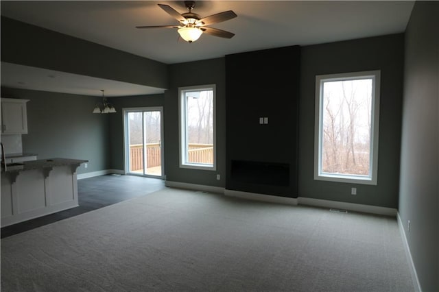 unfurnished living room featuring ceiling fan with notable chandelier and light carpet