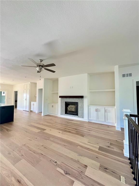 unfurnished living room with built in features, ceiling fan, a textured ceiling, and light hardwood / wood-style floors