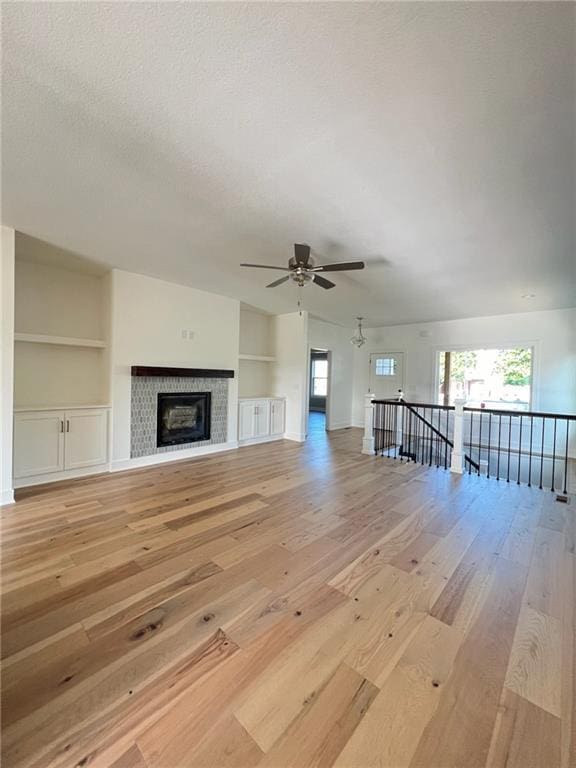 unfurnished living room with ceiling fan, light hardwood / wood-style flooring, built in features, and a textured ceiling