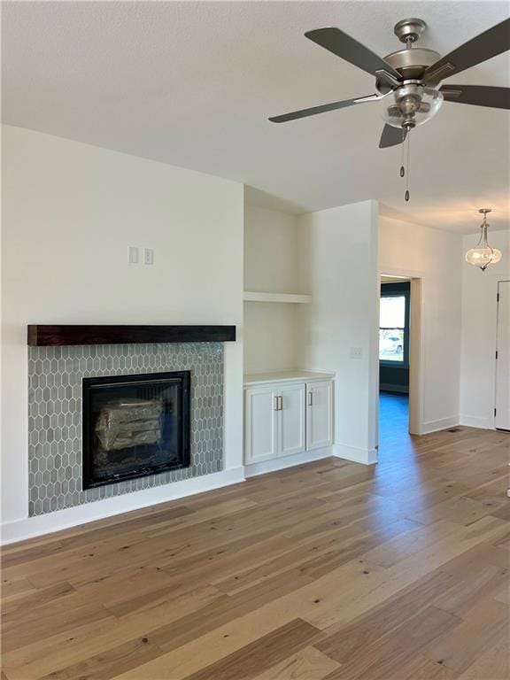 unfurnished living room featuring a tiled fireplace, light hardwood / wood-style floors, and ceiling fan