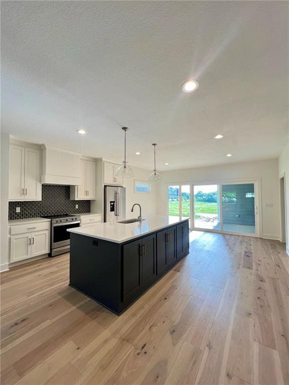 kitchen featuring white cabinetry, an island with sink, pendant lighting, stainless steel appliances, and light hardwood / wood-style floors