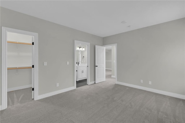 unfurnished bedroom featuring ensuite bathroom, light colored carpet, a closet, and a spacious closet