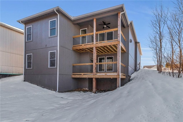 snow covered back of property featuring ceiling fan and a balcony