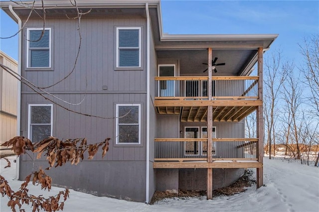 snow covered house featuring ceiling fan and a balcony