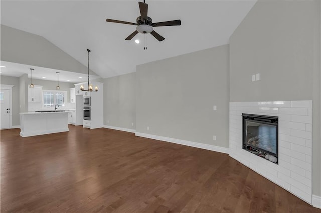 unfurnished living room with vaulted ceiling, a brick fireplace, sink, dark wood-type flooring, and ceiling fan with notable chandelier