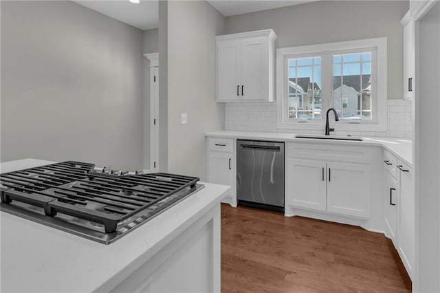 kitchen with white cabinetry, hardwood / wood-style floors, appliances with stainless steel finishes, decorative backsplash, and sink