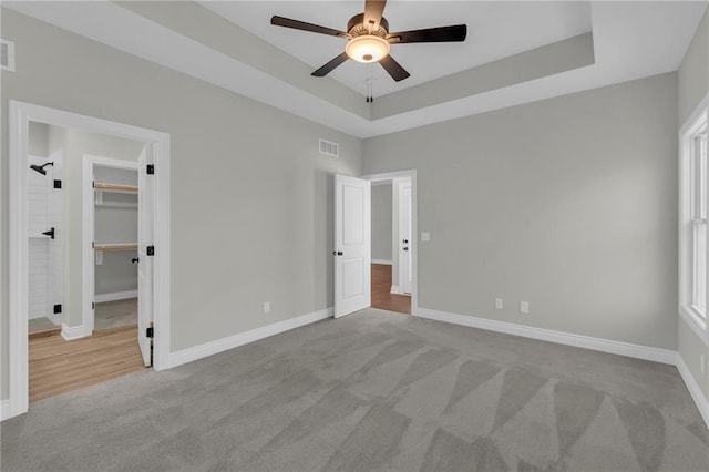 unfurnished bedroom with ceiling fan, light carpet, a spacious closet, and a tray ceiling