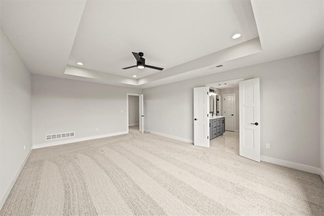 unfurnished bedroom with ceiling fan, connected bathroom, light colored carpet, and a tray ceiling