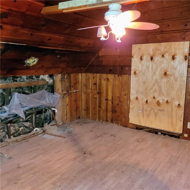 interior space featuring hardwood / wood-style floors, lofted ceiling, ceiling fan, and wooden walls