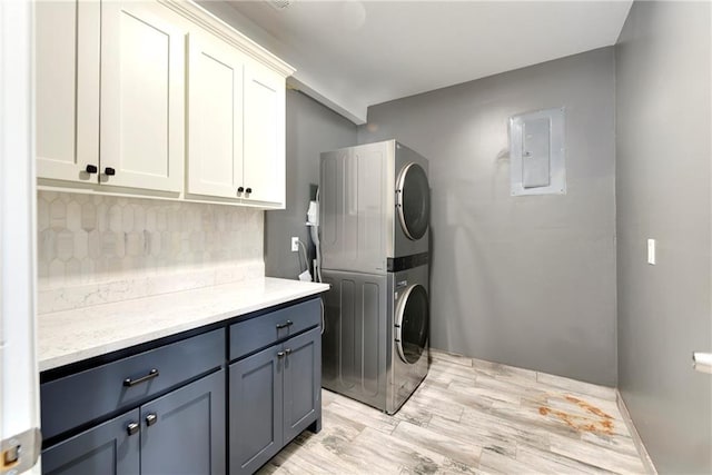 laundry area with stacked washer and clothes dryer, light wood-type flooring, and cabinets