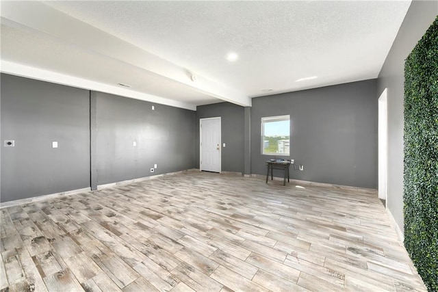 spare room featuring beam ceiling, a textured ceiling, and light hardwood / wood-style flooring