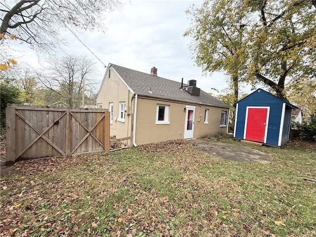 6133 Walrond Ave, Kansas City, MO 64130 - rear view of property featuring a storage unit, stucco siding, an outbuilding, fence, and a chimney