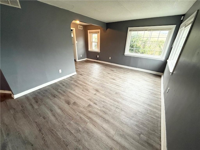 6133 Walrond Ave, Kansas City, MO 64130 - unfurnished bedroom with arched walkways, visible vents, multiple windows, and wood finished floors