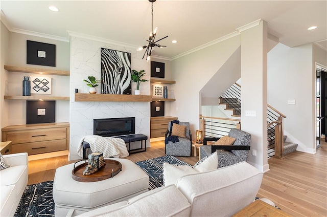 living room featuring ornamental molding, light hardwood / wood-style flooring, a notable chandelier, and a large fireplace