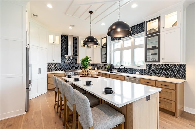 kitchen featuring wall chimney range hood, white cabinets, light wood-type flooring, and a kitchen island