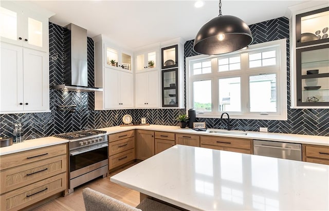 kitchen with wall chimney range hood, backsplash, sink, pendant lighting, and stainless steel appliances