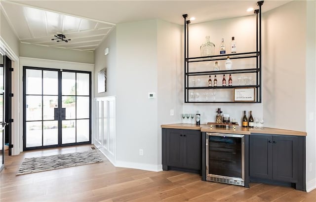 bar with light hardwood / wood-style floors, wood counters, and beverage cooler