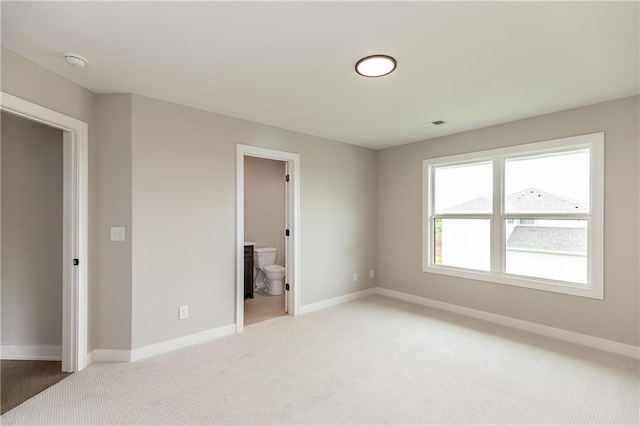 unfurnished bedroom featuring light colored carpet and ensuite bath