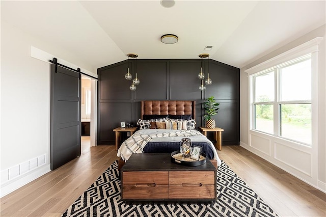 bedroom with lofted ceiling, a barn door, and light wood-type flooring