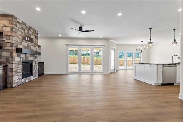 unfurnished living room featuring wood-type flooring, ceiling fan with notable chandelier, sink, and a fireplace