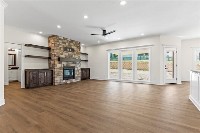 unfurnished living room featuring ceiling fan, ornamental molding, dark wood-type flooring, and a stone fireplace