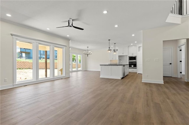 unfurnished living room featuring wood-type flooring, ceiling fan with notable chandelier, and sink