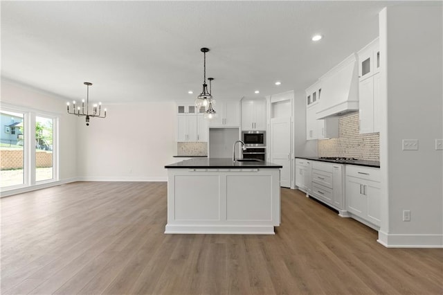 kitchen featuring white cabinetry, hardwood / wood-style floors, custom range hood, appliances with stainless steel finishes, and tasteful backsplash