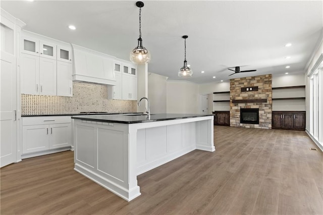 kitchen with backsplash, an island with sink, white cabinets, a fireplace, and hardwood / wood-style floors