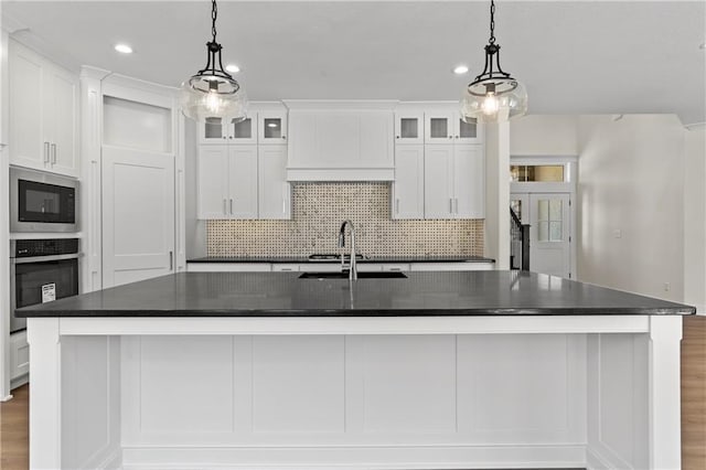 kitchen with appliances with stainless steel finishes, sink, backsplash, hardwood / wood-style floors, and a kitchen island with sink