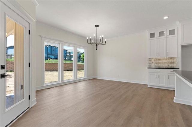 unfurnished dining area featuring ornamental molding, an inviting chandelier, and light hardwood / wood-style floors