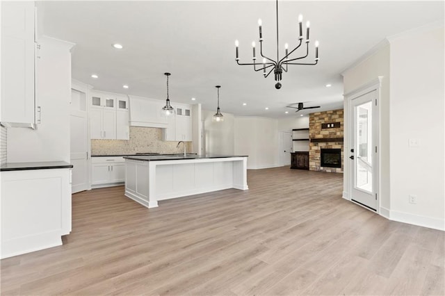 kitchen with a stone fireplace, decorative light fixtures, white cabinets, and light wood-type flooring