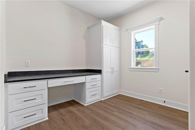 unfurnished office featuring hardwood / wood-style floors and built in desk