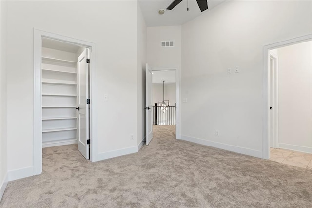 unfurnished bedroom with a closet, a spacious closet, a towering ceiling, light colored carpet, and ceiling fan